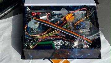 A black box houses an electronics kit with an ESP32 microcontroller, temperature sensor, multicolored ribbon cable, and LCD display being assembled for the "Onca" project. The components shown represent the hardware integration work mentioned in the day 2 build update for the Superteam Brasil x ZeroClaw bounty.