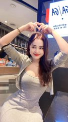 The image features a woman wearing a gray dress sitting at a table or counter. She has her arms up in the air, forming a heart shape with her hands. The background of the image shows a store or restaurant setting, which adds context to the scene.