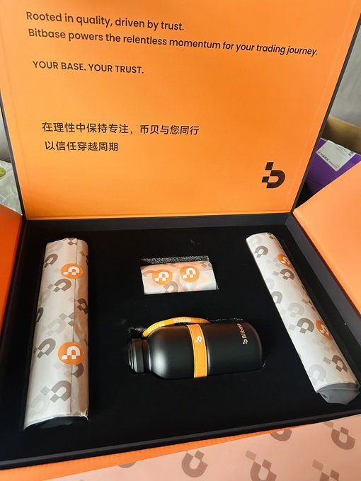 An open orange Bitbase promotional gift box reveals a black thermos, a small card, and patterned tissue-wrapped items, with the inside lid displaying "Rooted in quality, driven by trust" and the slogan "Crossing cycles with trust" (以信任穿越周期). The contents align with the post's appreciation of Bitbase's practical merchandise—useful daily items rather than decorative pieces—while the printed slogan directly echoes the phrase highlighted in the caption.