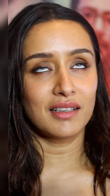 A close-up portrait photograph of a young woman with long dark hair looking to the side with a subtle expression, showing detailed eye makeup.