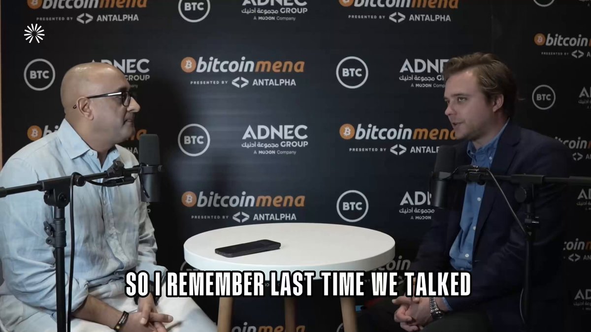 The image features two men sitting across from each other at a table with microphones, appearing to be having a conversation or participating in an interview. The background includes a black wall adorned with various logos, including one for Bitcoin. The text on the image reads "Silent payments on @solana inspired by Bitcoin silent payments. Quick context on how BTC silent payments work. You publish one static address that you can share anywhere. But every time someone pays you, the funds don'". This suggests a connection between the two men's conversation and the concept of Bitcoin transactions or silent payments.