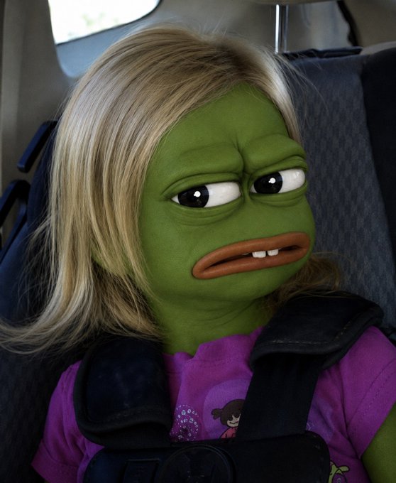 A person with a green ogre-like face filter, wearing a blonde wig and a purple shirt, sits in a car seat secured by a black seatbelt with a unamused expression.