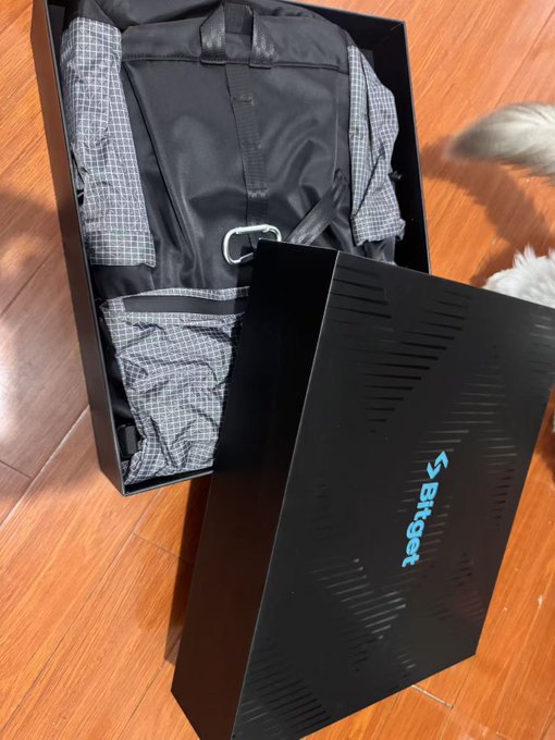 A black Brigear backpack sits in its branded box on a wooden floor, with a dog's tail visible in the corner. The image accompanies a post reflecting on the importance of documenting industry experiences and connections earlier, with the post's text cut off mid-sentence.