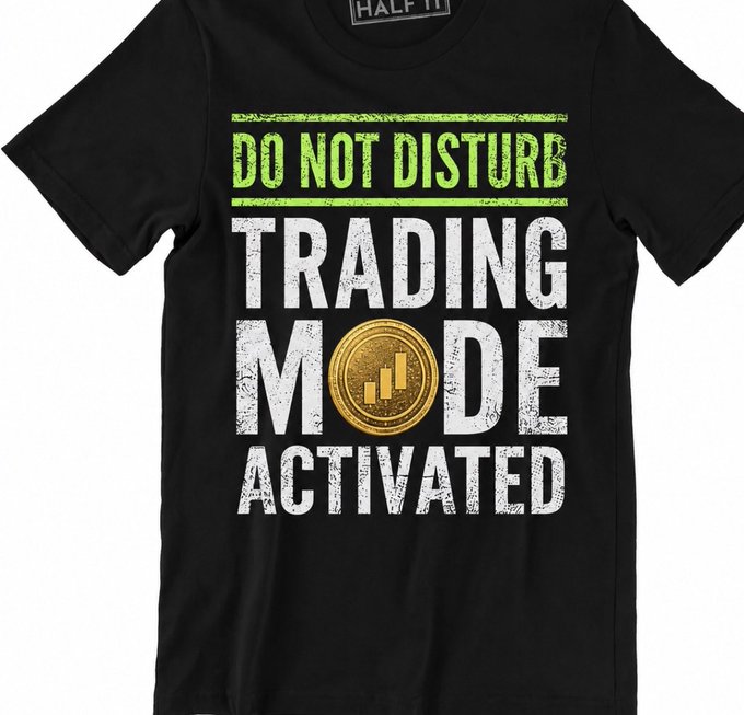 A black T-shirt features green-and-white distressed text reading “DO NOT DISTURB / TRADING MODE ACTIVATED,” with a gold coin-style meme symbol. It previews a memecoin-themed merch collection designed to build retail excitement.