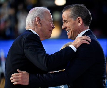The image shows two men dressed in suits, one older man with white hair wearing a suit jacket and the other younger man wearing a suit as well. They are both smiling at each other while hugging their shoulders. The caption of the image reads "Son of President Biden likes bitcoin".