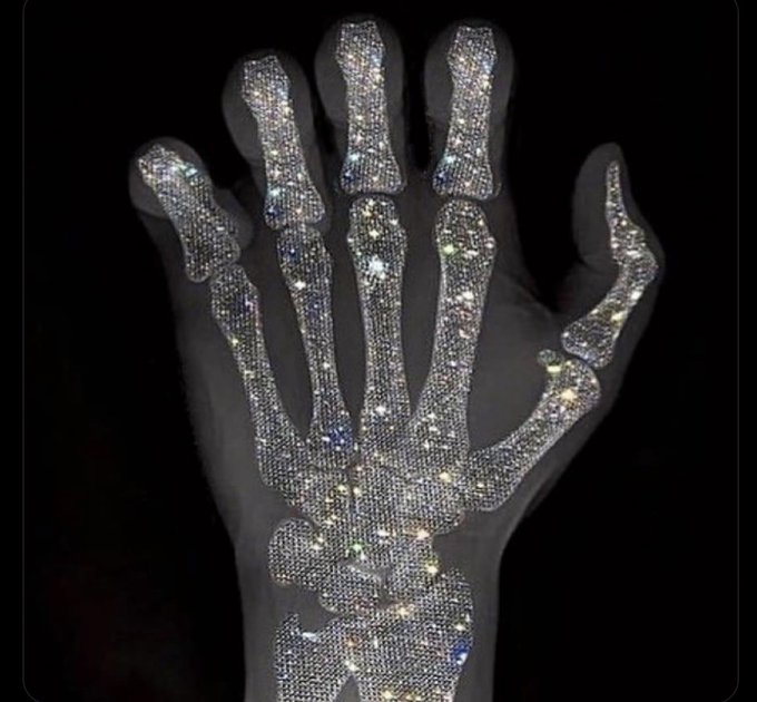 An X-ray style image of a human hand skeleton overlaid with sparkling, diamond-encrusted patterns on a black background.