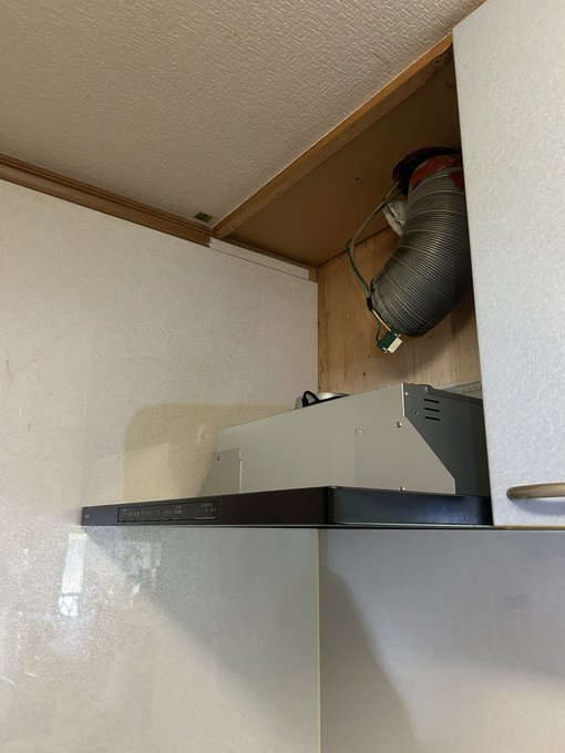 An installation view inside a cabinet shows a grey range hood and a corrugated silver exhaust duct connecting to the wooden back panel.