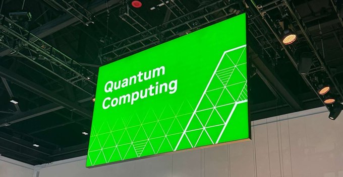The image features a large screen displaying a green banner with white text, which reads "Quantum Computing" along with the phrase "Today's applications will demand more than speed. They'll demand intelligent computation." The banner is hanging from the ceiling of an event space and is positioned above a stage where a speaker can be seen.

The image also includes some text that says "@quipnetwork is preparing for that future today". This suggests that the event might be related to Quantum Computing or technology in general, with a focus on the advancements and potential applications of intelligent computing systems.