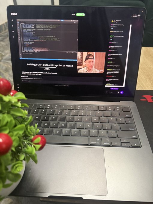 A laptop on a desk displays a live stream titled "Building a CoFi/Defi Arbitrage Bot on Monad AMA," showing code on screen and a man with a cap in the webcam feed, while the live chat scrolls with viewer comments—visually tying into the post's tease of upcoming alpha, giveaways, and partnership news.