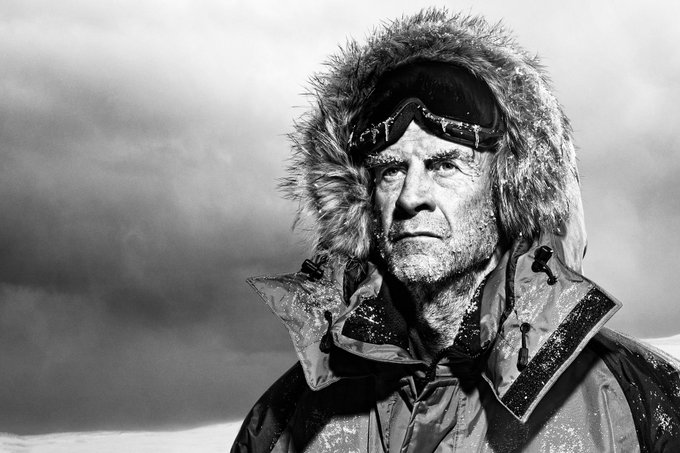 A black-and-white close-up portrait shows a rugged, weathered man wearing a fur-lined hooded parka and goggles pushed up on his forehead, with frost and snow visible on his face and jacket, set against a desolate, overcast backdrop. The image visually embodies the post's message about emotional steadiness under extreme conditions, mirroring the stoic resilience Sir Ranulph Fiennes sought in his polar team—and the mindset needed to stay calm through Bitcoin's volatile bull and bear cycles.