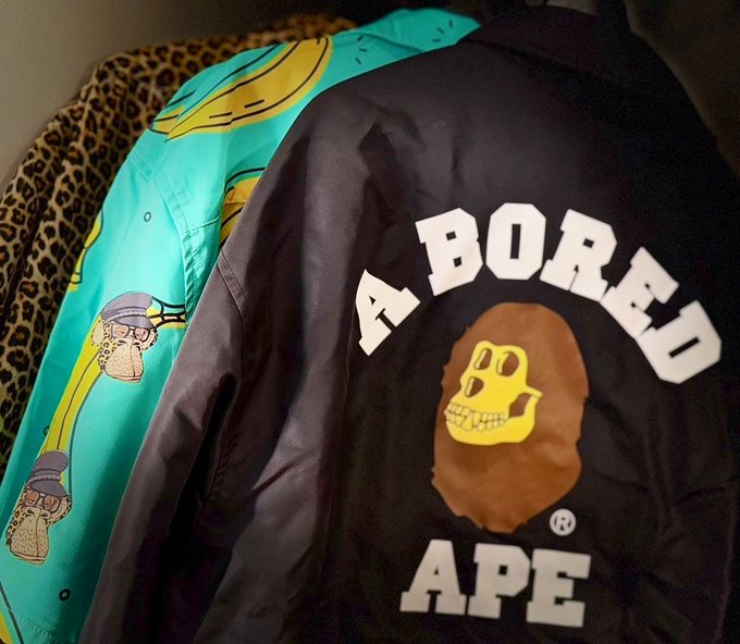 A black satin jacket with 'A BORED APE' text and the iconic yellow Bored Ape skull logo is draped next to a teal Banana-themed jacket with cartoon characters.