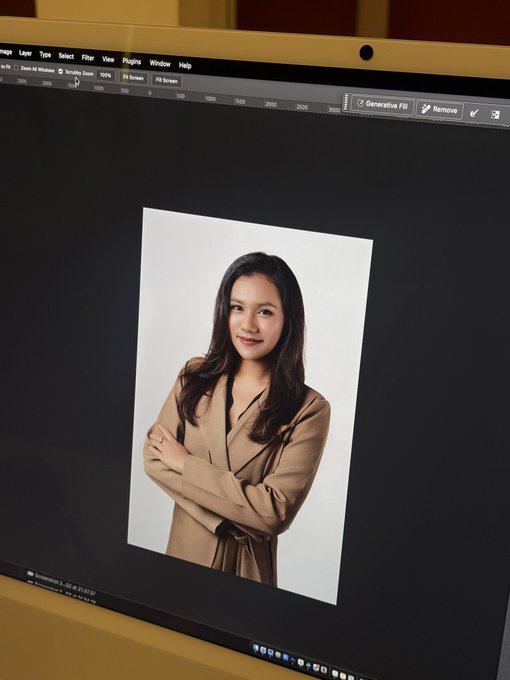 A computer monitor displaying Adobe Photoshop (Generative Fill feature visible) showing a professional portrait photo of an Asian woman with long hair, wearing a tan/beige blazer and posing with crossed arms against a white background.