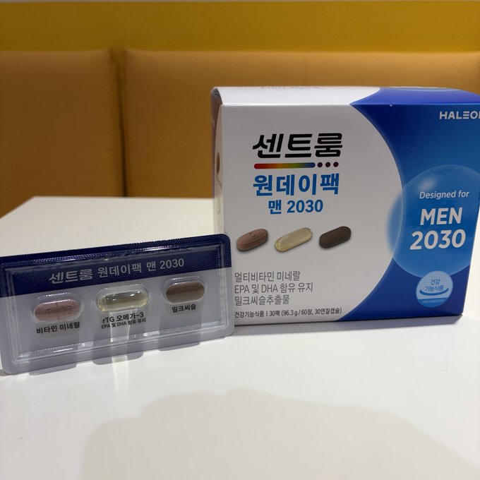 A Korean health supplement product "센트룸 원데이 팩 맨 2030" (Centrum One-Day Pack Men 2030) by Haleon is displayed on a white table, showing its packaging box alongside a blister pack containing three different colored tablets labeled 비타민 미네랄 (Vitamins & Minerals), 오메가-3 (Omega-3 EPA & DHA), and 밀크씨슬 (Milk Thistle). The image appears to be a clear product photo shared in response to a question about whether the post is a backdoor advertisement, directly showcasing the branded supplement as advertised.
