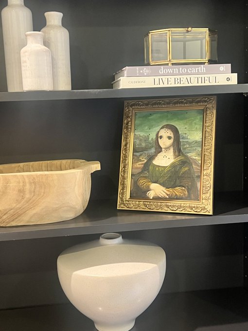 A dark bookshelf displays books titled 'down to earth' and 'LIVE BEAUTIFUL' alongside a small framed print of the Mona Lisa, a wooden bowl, and various decorative vases.