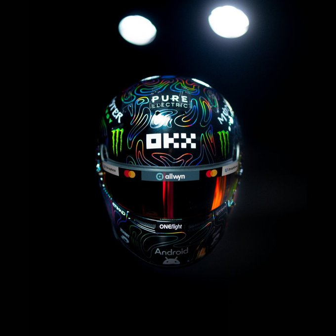 A new Formula 1 helmet is revealed against a dark background, featuring a vibrant rainbow-topographic design with sponsor logos including "OKX," "Monster," "Pure Electric," "Allwyn," "Android," and "ONE//light." The post "We're so back. Rate the new lids." suggests this is a debut reveal of a driver's new race helmet, likely from the 2025 season.