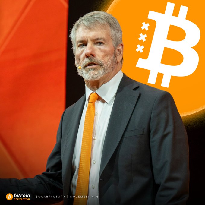 A man in a dark suit with an orange tie speaks at the Bitcoin Amsterdam 2024 conference (SugarFactory, November 5-6) against a backdrop featuring the Bitcoin logo.