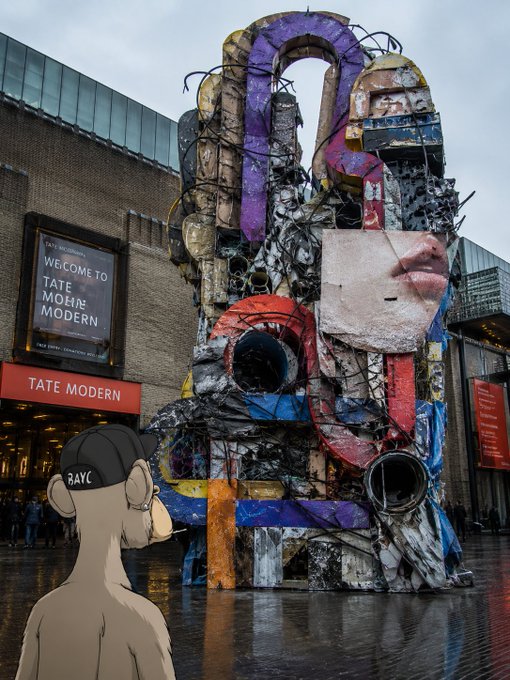 A large, colorful, abstract sculpture resembling a fragmented human face stands outside the Tate Modern, with a 'WELCOME TO TATE MODERN' sign and an animated monkey character wearing a 'RAYC' cap observing it.