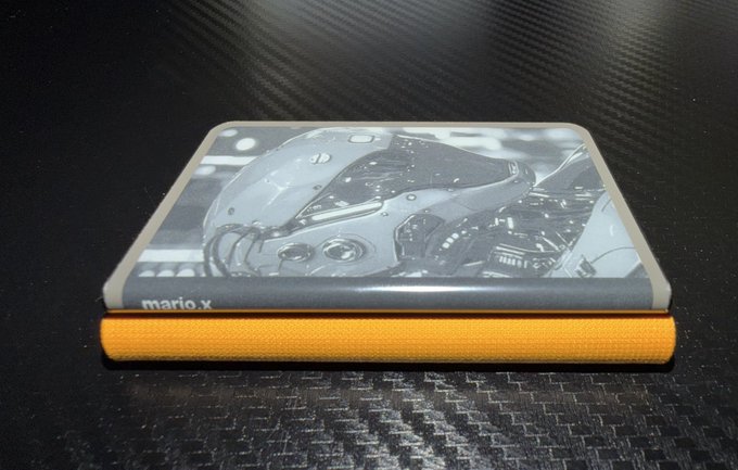 Two stacked notebooks on a dark surface, the top one featuring a motorcycle design with 'mario.x' text, resting on an orange fabric-covered notebook.