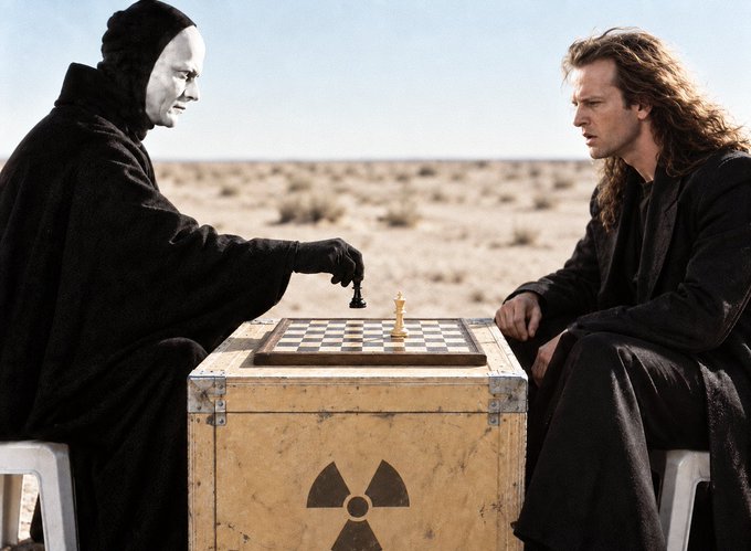 Two figures in black robes, one wearing a pale mask, sit across from each other at a wooden crate marked with a radiation symbol, playing chess in a barren desert landscape.