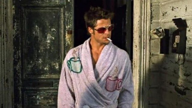 A man with tousled hair wears red-tinted sunglasses and a light blue bathrobe decorated with embroidered mugs, with a cigarette dangling from his lips as he stands in a doorway. The "Gm winners" post humorously frames this iconic, effortlessly cool image—reminiscent of Brad Pitt's Tyler Durden from *Fight Club*—as the epitome of a winning morning look.