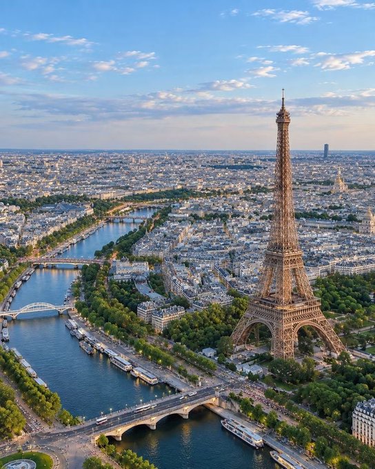 An aerial view of Paris showing the Eiffel Tower prominently in the foreground with the Seine River winding through the city and bridges crossing it.