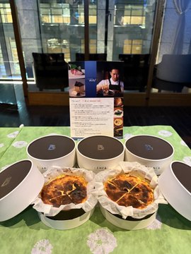 Four round containers of soup and two open pies/galettes on a table with a green tablecloth, with a food menu visible in the background.