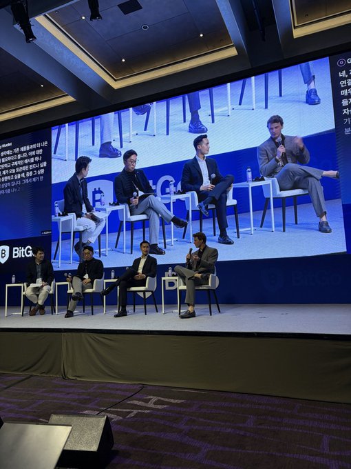 A panel discussion event on stage with five men seated in white chairs, featuring BitGo branding, with a large screen behind them displaying the panelists and Korean text.