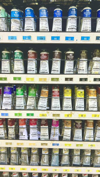 A store shelf displaying organized rows of numbered paint cans and tinting bottles, primarily branded 'Tinta a Oleo CORFIX' with color-coded labels.
