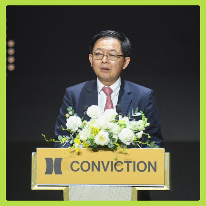 Deputy Prime Minister Hồ Quốc Dũng, wearing a navy suit and red tie, delivers a speech at the "CONVICTION" podium adorned with white flowers at the Conviction 2026 event's opening ceremony on August 14.