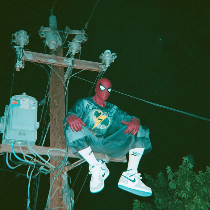 A figure in a Spider-Man mask paired with Nike Air Jordan 1 sneakers sits perched on a utility pole, blending streetwear and superhero aesthetics. The image symbolizes the "HYPE" crypto airdrop narrative—capturing the surreal, larger-than-life positioning required to capitalize on Hyperliquid's massive ecosystem liquidity event.