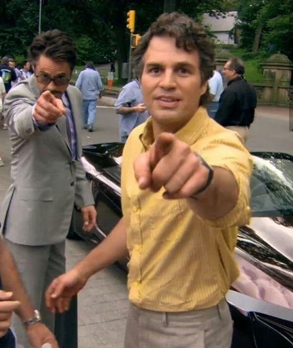 The image features a man wearing a yellow shirt pointing at something or someone while standing next to another person dressed in a suit, possibly an actor. The background includes trees and cars, suggesting that they are in an outdoor setting with some form of transportation nearby. The caption reads "I'LL BE HOPEFUL ON @xomarket's 50K WORLD CUP PARLAY AND WITH ZERO fees, I get to keep more of what i make." This implies that the man is excited about a new project or event and wants to share his enthusiasm with others.