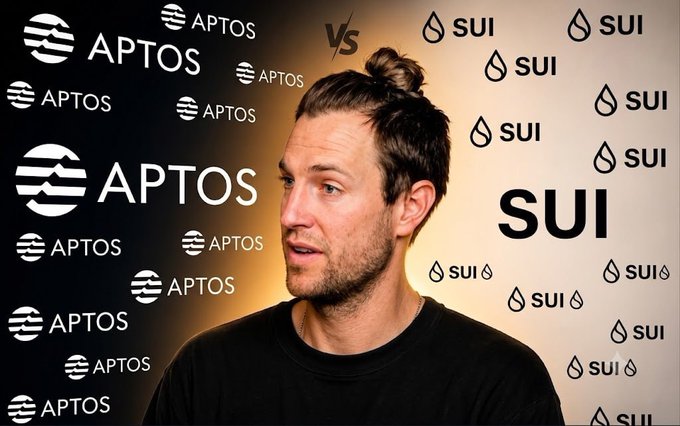 A man with a man bun speaking in front of a backdrop featuring the logos for 'APTOS' and 'SUI' separated by 'VS'.