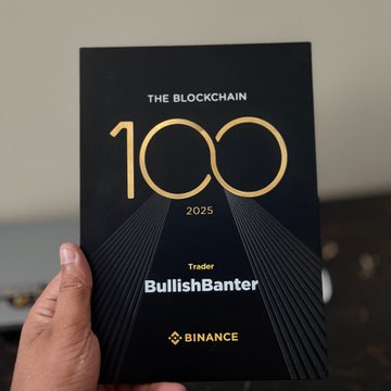 The image shows a person holding up an award-winning book with the title "The Blockchain 100" on a black background, which is set against a white background. The hand appears to be positioned near the bottom left corner of the book.