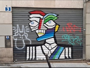 A colorful graffiti mural of a stylized face on a metal roll-up door, with the number '3' visible on a nearby blue sign.
