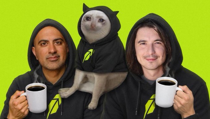 Two men and a cat, all wearing matching black hoodies with a green lightning bolt logo, pose against a bright green background while holding mugs of coffee.