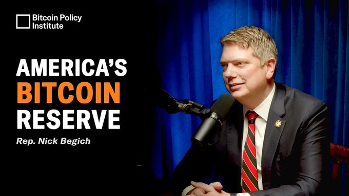 The image features a man wearing a suit and tie sitting behind a microphone, giving him an air of authority or expertise. The background shows a blue curtain with the text "America's Bitcoin Reserve" written above the man's head. This suggests that he is discussing or advocating for the idea of treating Bitcoin as a strategic reserve asset, similar to how gold has been historically used in times of economic uncertainty.