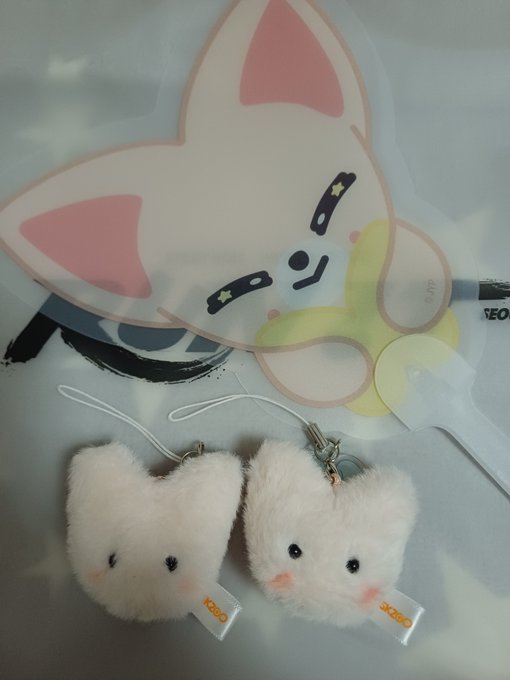 Two white fluffy cat face keychains hang below a cute pink-eared cartoon cat sticker.