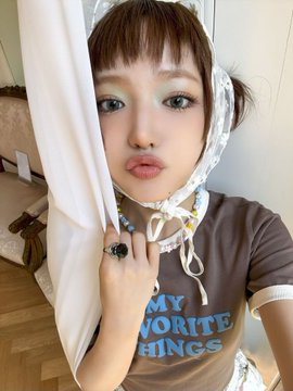 A person wearing a lace headpiece and a brown shirt with 'MY FAVORITE THINGS' printed on it makes a pouting expression while pulling a white curtain.