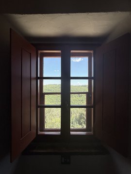 The image shows a window with two open wooden doors, offering a view of a beautiful landscape outside. The scene appears to be set in Tuscany, Italy, as indicated by the presence of a hillside view. The photo has been captioned "Two days offline in Tuscany was the break I didn’t know I needed. Monitoring the situation 24/7 will fry you, touch grass occasionally Now packing for the Hyperliquid Amsterdam event tomorrow." This post seems to be about an upcoming trip or vacation and is likely related to travel experiences or recommendations.