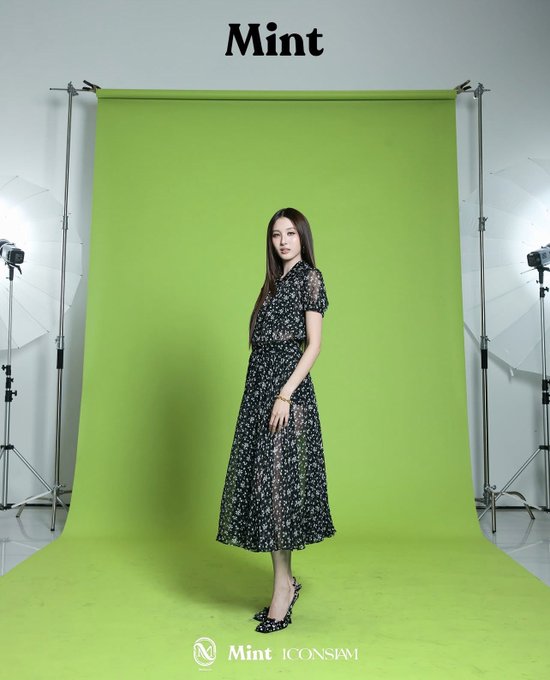 A woman with long dark hair poses in a black floral dress against a vibrant green backdrop in a photography studio setup with visible lighting equipment on both sides, while the text "Mint" appears at the top and "Mint ICONSiam" is displayed at the bottom, tying into the post's promotional content for the MChoice Mint Awards 2026 featuring Benyapa.