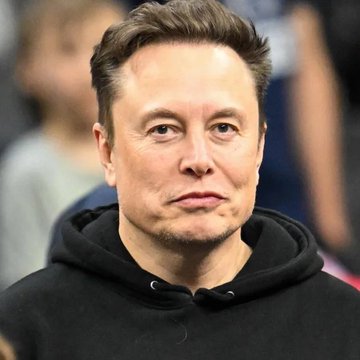 The image shows Elon Musk wearing a black hoodie, with a blurred crowd in the background. The accompanying post’s phrase “Translation: Bitcoin” appears to interpret or connect the image to cryptocurrency Bitcoin, though no Bitcoin symbol, ticker, or other text is visible.