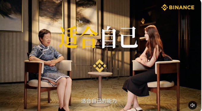 A still from a video titled '适合自己' (Suit Yourself) featuring a Binance logo, showing an older woman in a cheongsam and a younger woman in a black dress sitting in armchairs across from each other in an interview setting.