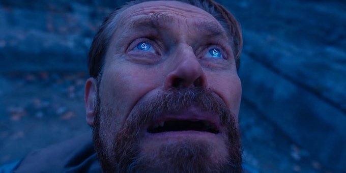 A close-up shot of a bearded man with glowing blue eyes looking upward with a pained or emotional expression in a blue-toned scene.