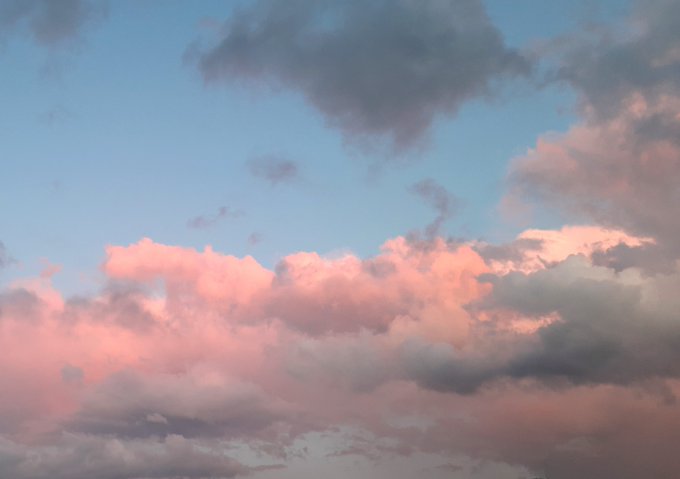A serene sky at dusk or dawn with soft pink and blue clouds scattered across a pale blue background.