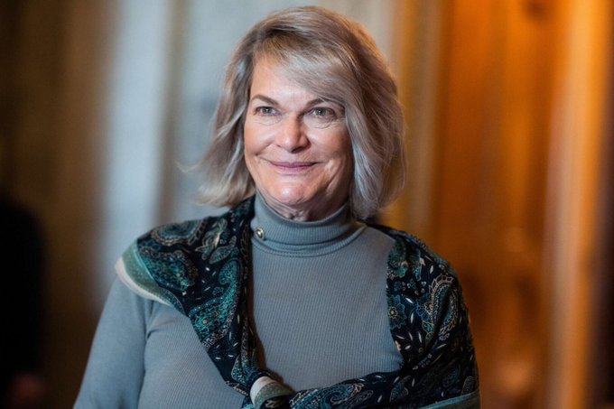 The image features a woman with short blonde hair wearing a gray shirt and a blue and black paisley scarf around her neck. She has a warm smile as she looks directly at the camera, giving off an air of confidence and approachability. The caption provided in the image is related to the topic of cryptocurrency, specifically discussing the importance of the CLARITY Act for protecting crypto investors. This act ensures that users have the right to know if they are investing their money on a failed exchange or not, which can be crucial when it comes to safeguarding their digital assets and ensuring proper ownership rights.