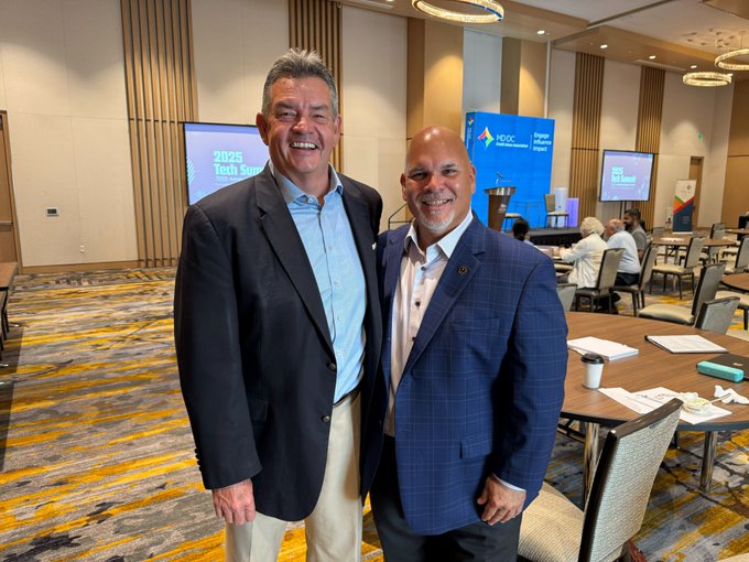 Two smiling men pose together at what appears to be a credit union industry event, with visible signage referencing "MD|DC" and "2026 Tech Summit" in the background, aligning with the post's announcement about the MD|DC CUA merger with The League expanding Metallicus and Metal Blockchain's reach across credit unions.