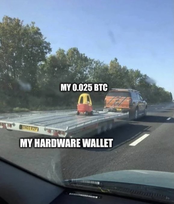 A meme showing a flatbed truck on a highway carrying a tiny toy car, with the text 'MY 0.025 BTC' labeling the toy and 'MY HARDWARE WALLET' labeling the flatbed.