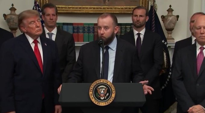 A man speaks at a podium bearing the seal of the President of the United States, flanked by several men in suits including Donald Trump. The image appears unrelated to the accompanying post about Chainlink cryptocurrency, showing instead what looks like a political press conference.