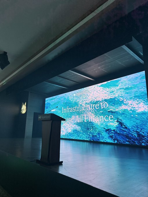 A conference stage at Hyperproof with a podium, featuring the text 'Infrastructure to use AI Finance' on a large screen displaying an ocean wave background.