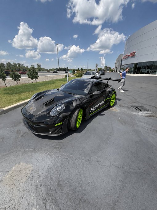 A black Porsche 911 GT3 RS with neon green accents and "Hypercraft" decals is parked outside a dealership, paired with a post tagging @novogratz and referencing $GLXY-themed custom car designs. The post suggests a playful idea of wrapping or customizing the hypercar with Galaxy Digital ($GLXY) branding, fitting the bold green-and-black color scheme already featured on the vehicle.